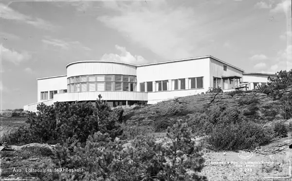 Historiskt svartvitt foto av Löftadalens folkhögskola på en klippa omgiven av buskar och tallar.