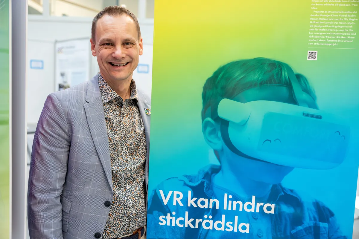 Medelålders man står vid en färgglad skylt och ler brett