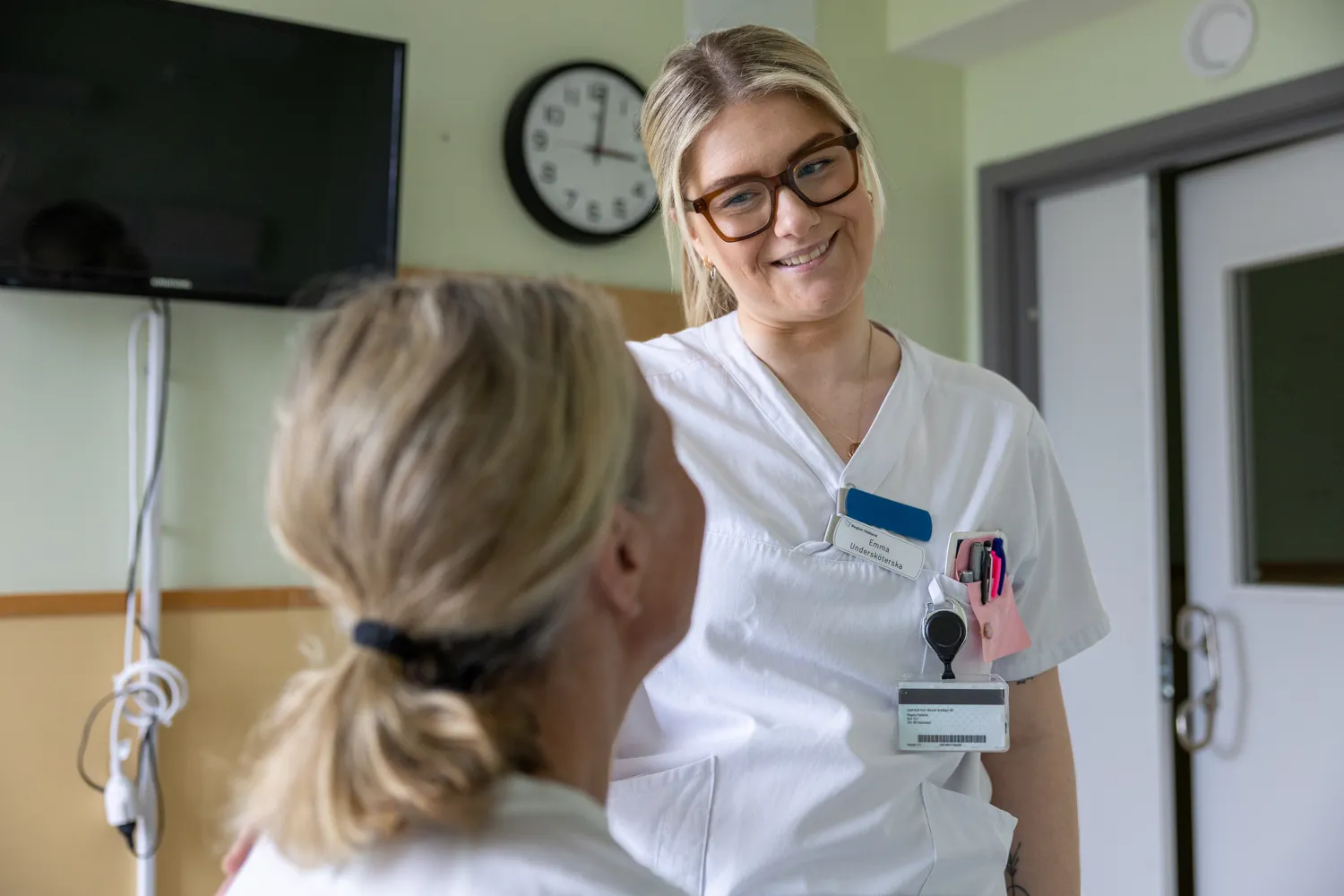 En ung kvinna i vita sjukhuskläder pratar med patient