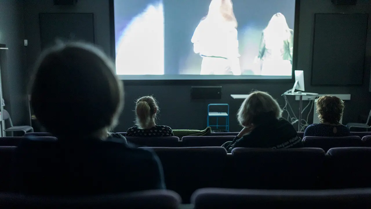 Fyra personer sitter i en mörk biosalong och tittar på en film på en stor duk.