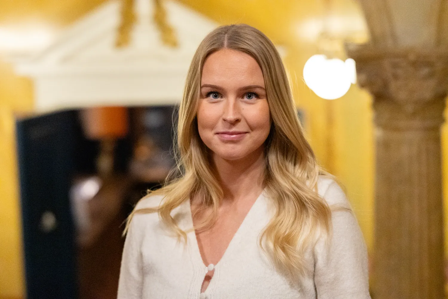 Ung kvinna står och ler framför kameran