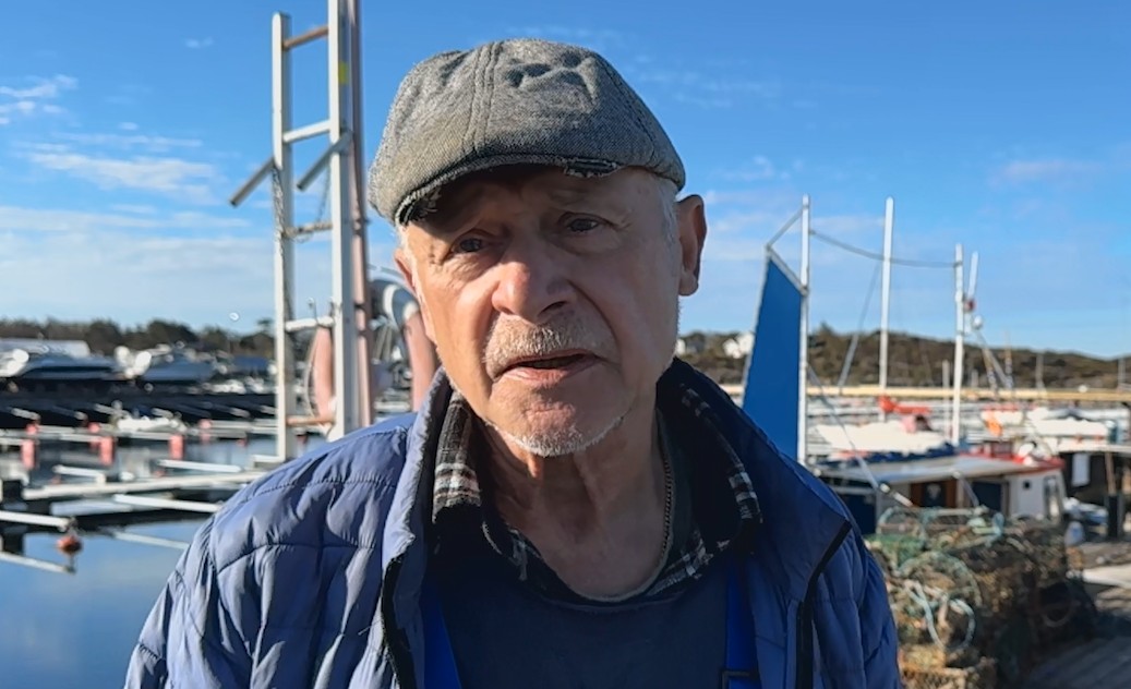 Äldre yrkesfiskare med keps som står på kajkant