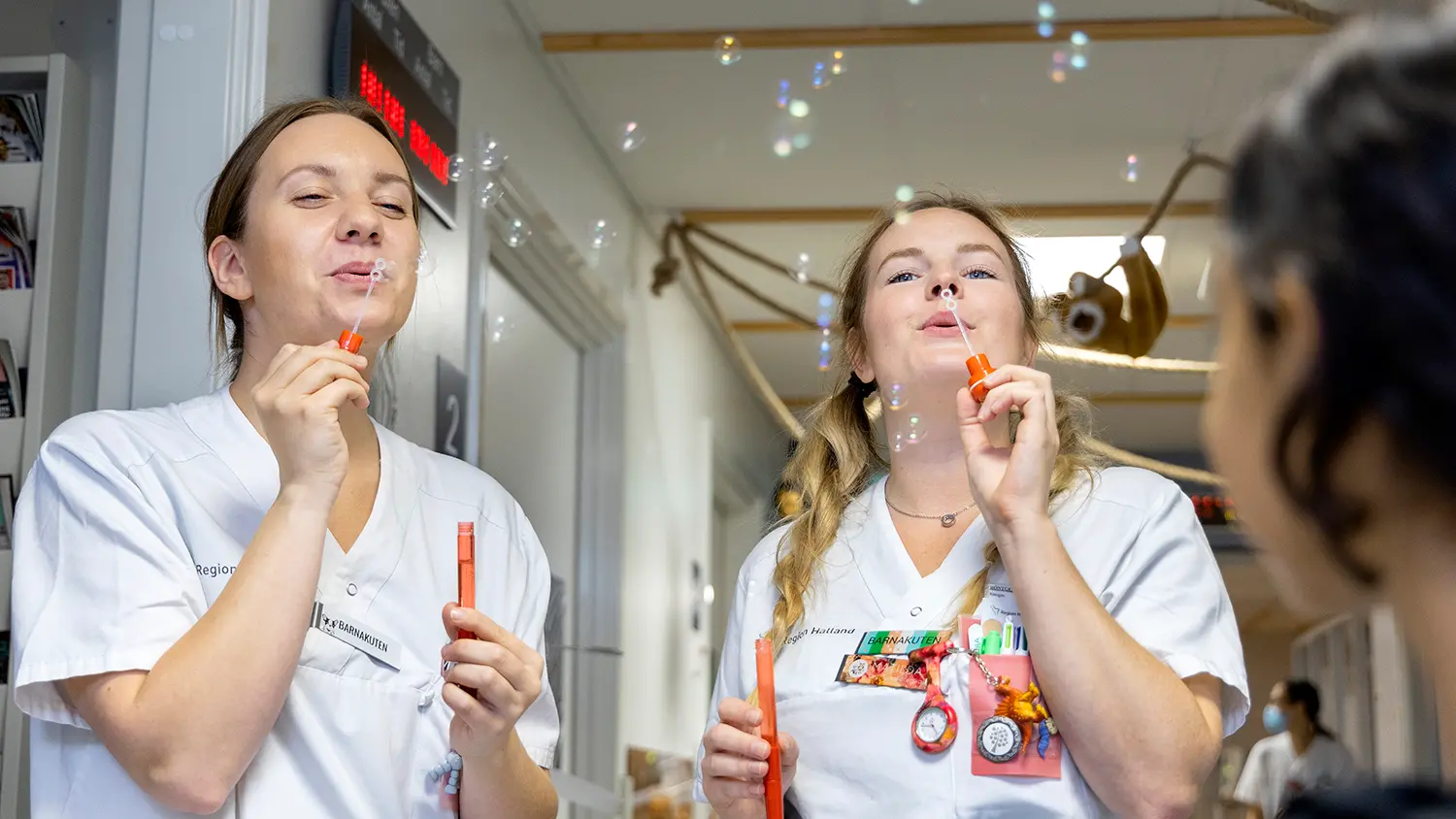 Två personer i vårdkläder blåser bubblor.
