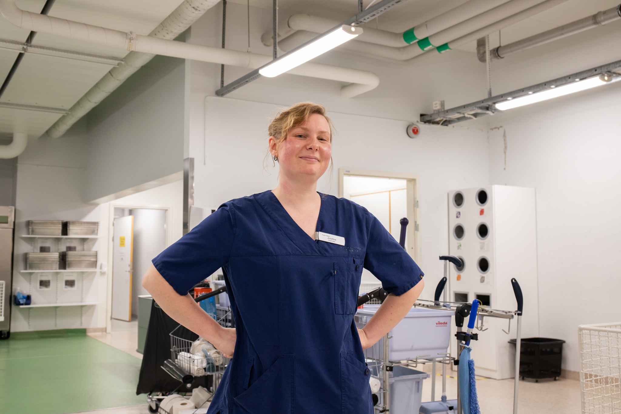 En kvinnlig städerska står med händerna i sidan och ler in i kameran