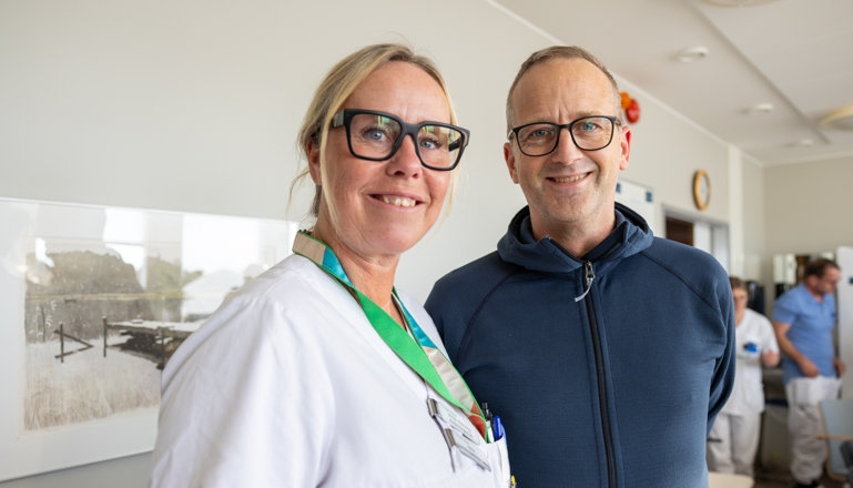 Två vårdpersonal, en kvinnlig och en manlig ler och tittar in i kameran