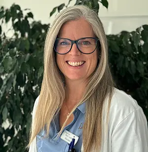 Leende kvinna med glasögon, långt hår och sjukhuskläder