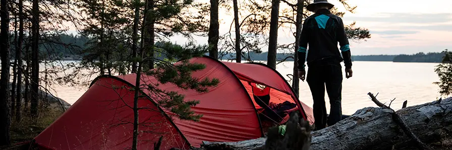 En person framför ett tält vid en sjö.
