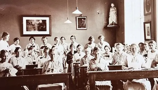 Ett äldre svartvitt fotografi av en skolklass som lyssnar och läser i sina böcker.