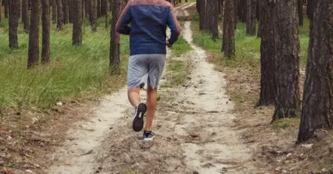 En man i hoodie och shorts springer på en skogsväg.