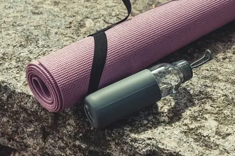 En yogamatta och en vattenflaska ligger på stenig mark.