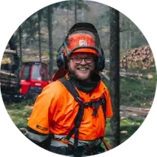 En man i orange skyddskläder och hjälm i ett skogsbruk.
