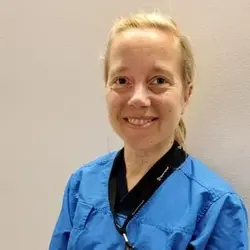 Leende blond kvinna i blå vårdkläder.