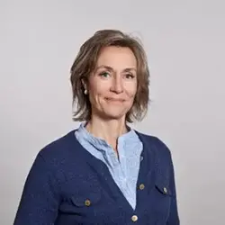 Leende mörkblond kvinna klädd i ljusblå skjorta och mörkblå kofta.