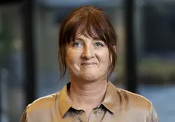 Leende mörkhårig kvinna klädd i kopparfärgad blus.