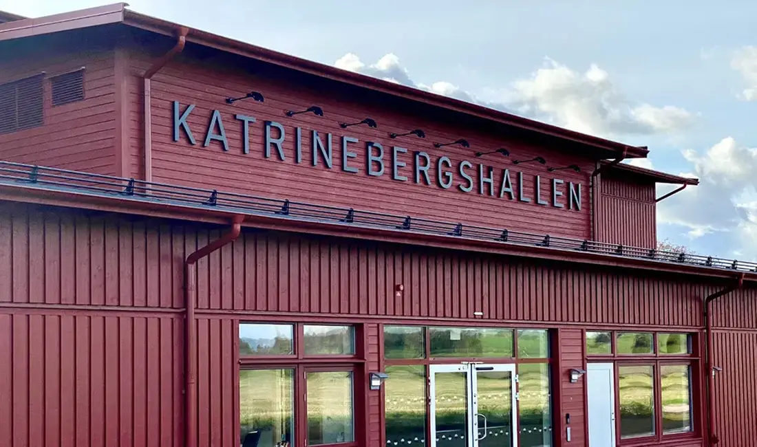 Katrinebergs folkhögskolas idrottshall. En röd träbyggnad med skylten "Katrinebergshallen".