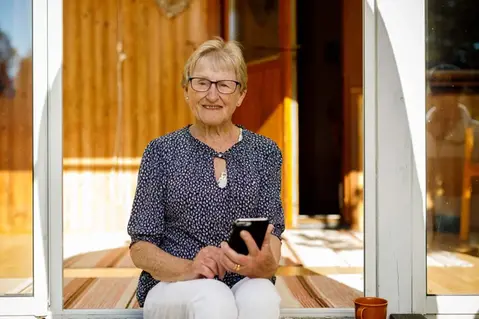 En äldre person sitter på en utomhustrappa, håller i en mobiltelefon.